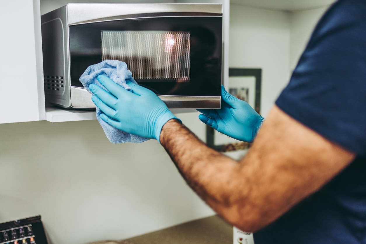 A man cleaning outside of a microwave using a microfiber cloth