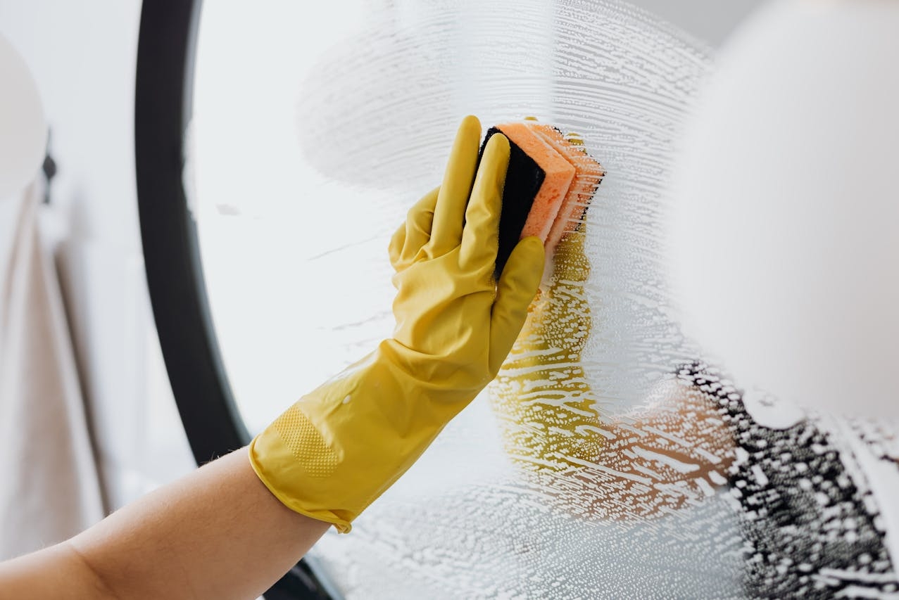 Cleaning person uses a glass cleaner to clean a mirror with latex gloves and a sponge